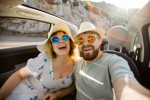 Romantic couple making selfie on smartphone camera in rental cabrio car on ocean or sea beach, enjoying summer vacation together and taking picture cellular resting near sea on weekends