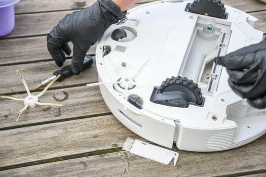 a woman unscrews the side brush from a robot vacuum cleaner with a screwdriver, routine maintenance of equipment for long-term use, high quality photo