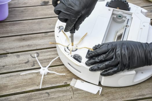 a woman unscrews the side brush from a robot vacuum cleaner with a screwdriver, routine maintenance of equipment for long-term use, high quality photo