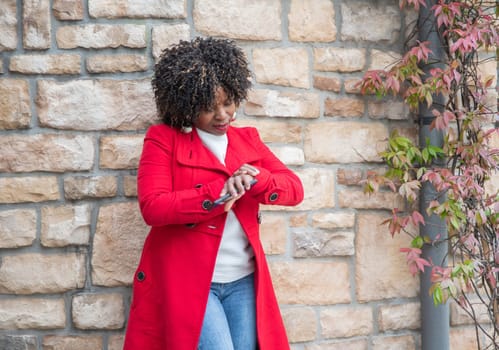 serious african american woman looks impatiently at her wrist watch near house while waiting for her husband, High quality photo