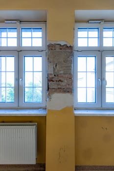 A pillar with peeling plaster between two windows inside an old abandoned hospital