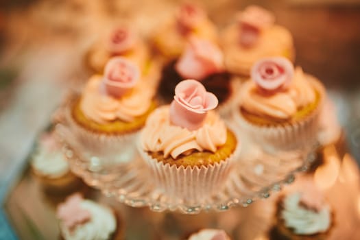 festive muffin with bright cream on glass stand. cupcake decorated with rose decor and cream, mini cake, pastries on a wooden background. cookie bar. High quality photo. selective focus.