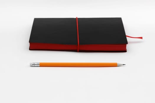 Orange pen on black leather moleskin notebook isolated on white