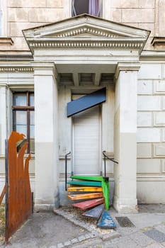 Entrance front of an old building with a black signboard and colored metal stairs