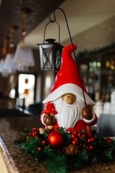 Fairy gnome with a Christmas lantern under the Christmas tree. Christmas decor in cafe. Christmas mood