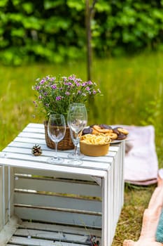 A green garden with a white wooden crate on which there are glasses, flowers and snacks in bowls