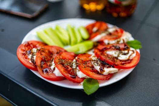 White plate full of cucumber slices and tomato slices and mozzarella cheese as a capreze salad