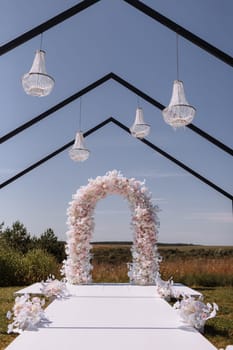 Place for wedding ceremony in garden outdoors. Wedding arch decorated with flowers and crystal chandeliers. Wedding setting