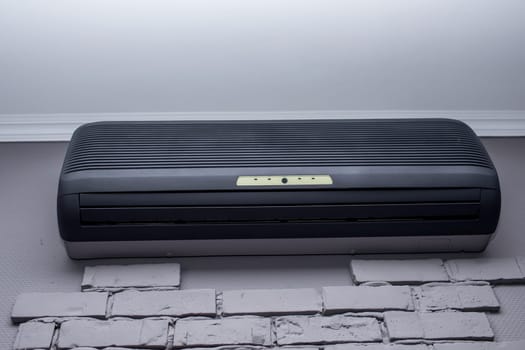 modern black air conditioner hanging on white brick wall. High quality photo.