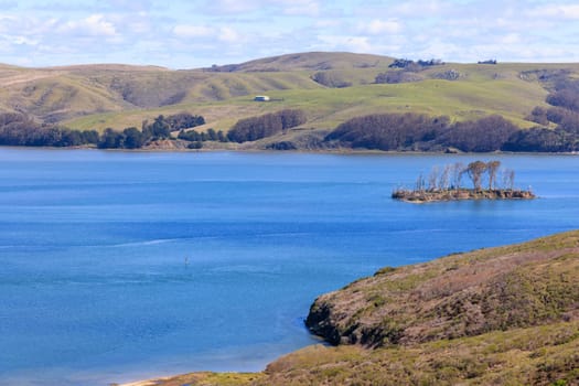 Small island in blue waters and rolling green hills on California coast. High quality photo