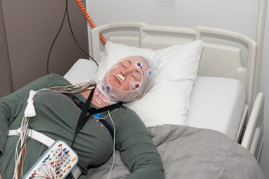 Middle aged woman measuring brain waves, examining polysomnography in sleep laboratory, High quality photo