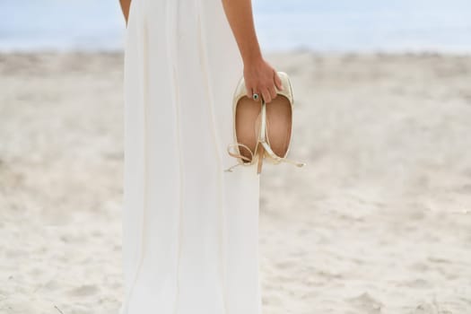 Bride in white dress and golden shoes on the sandy beach