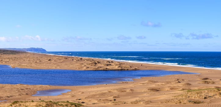 Blue lagoon on deserted sandy beach with Point Reyes cliffs in distance. High quality photo