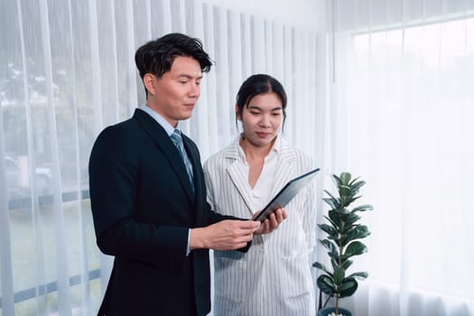 Manager advising guiding younger colleague with tablet in workplace. Couple businesspeople in formal wear working together on financial strategy as concept of teamwork and harmony in office.