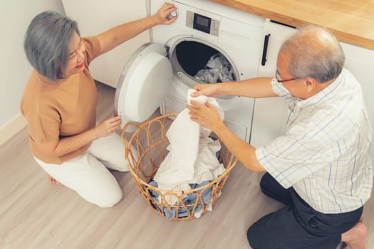 Senior couple working together to complete their household chores at the washing machine in a happy and contented manner. Husband and wife doing the usual tasks in the house.