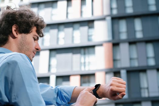 Young progressive businessman using touchscreen smartwatch to check time, browsing internet in city area. Concept of electric hand gadget feature with mobile app, physical heart rate and time.