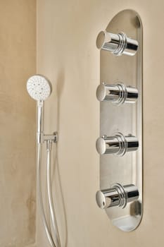 a wall mounted shower with two handsets and an overhead hand showerhead in the background is a tan colored wall