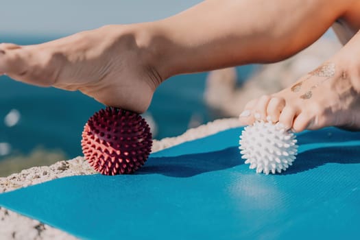 Middle aged well looking woman with black hair doing Pilates with the ring on the yoga mat near the sea on the pebble beach. Female fitness yoga concept. Healthy lifestyle, harmony and meditation.