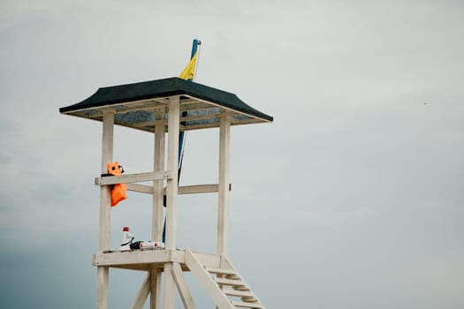 Empty white lifeguard tower with a yellow flag on the beach in windy weather. Beach lifeguard tower with yellow flag indicator. Nobody. Holiday recreation concept