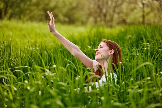happy, contented woman sitting in tall green grass enjoying a pleasant day with her arms raised high. High quality photo