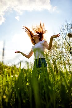 a happy woman in summer clothes stands in a field lit from behind and with her hair flying in the air. High quality photo