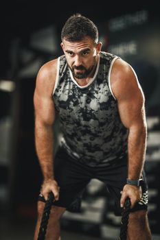 Shot of a muscular guy in sportswear doing exercises with ropes at the gym.