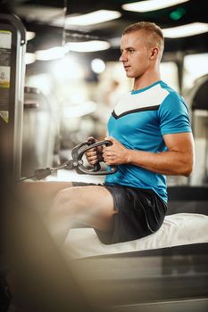 Shot of a muscular guy in sportswear working out at the hard training in the gym. He is pumping up back muscle with heavy weight.