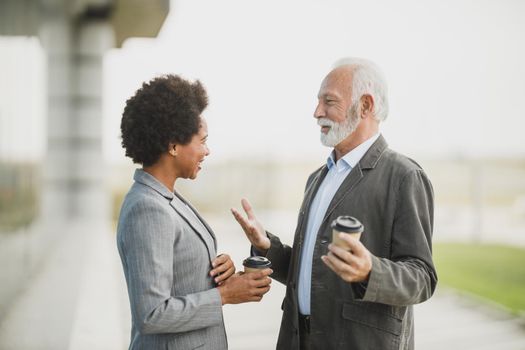 Shot of two successful multi-ethnic business people talking while having a coffee break in front of the office building.