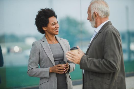 Shot of successful black businesswoman and her senior male colleague talking while having a coffee break outdoors.