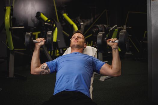 Shot of a muscular guy in sportswear working out at the hard training in the gym. He is pumping up chest muscule with heavy weight.