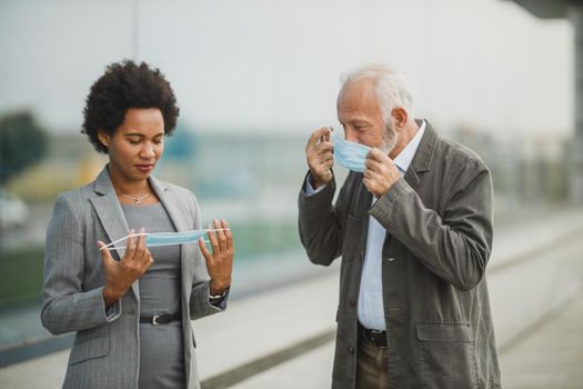 Shot of two successful multi-ethnic business people using protective mask while having a quick break in front of the office building during COVID-19 pandemic.