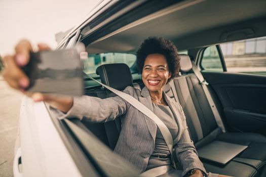 Shot of a successful black businesswoman taking selfie with smartphone while sitting in the backseat of a car during her morning commute.