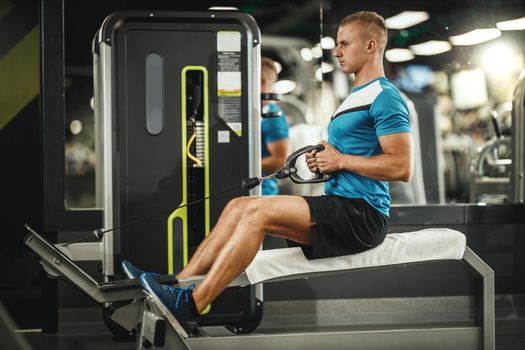 Shot of a muscular guy in sportswear working out at the hard training in the gym. He is pumping up back muscle with heavy weight.