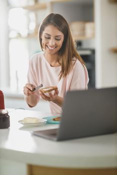 Shot of a young woman spreading butter onto toast in her kitchen.