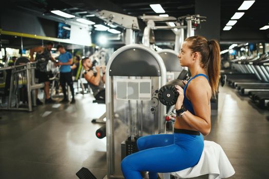 Shot of a muscular young woman in sportswear working out at the gym machine. 