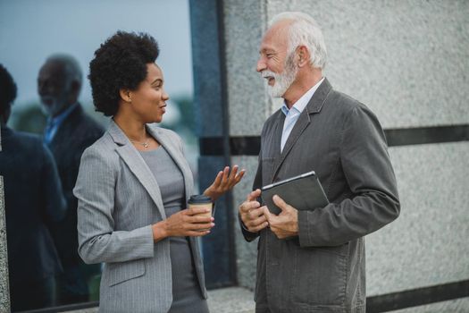 Shot of successful black businesswoman and her senior male colleague having a discussion during a coffee break in front of the office building.