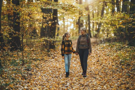 Shot of a teen girl and her mom walking together through the forest in autumn.