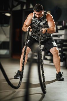 Shot of a muscular guy in sportswear doing exercises with ropes at the gym.