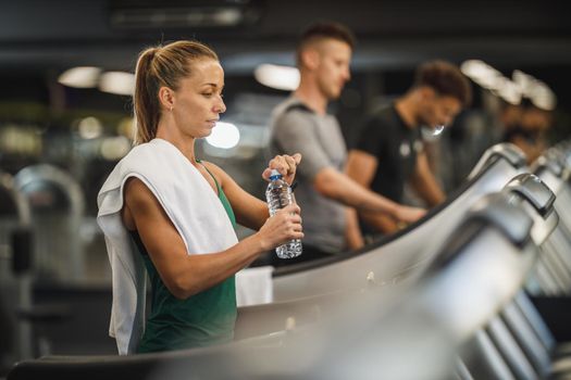 Shot of a young woman walking on a treadmill at the gym. She is getting to drink water.