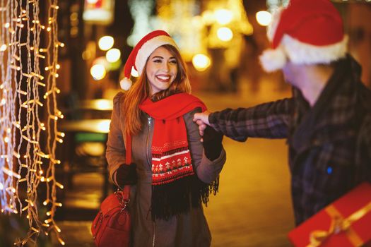 Shoot of a cheerful young couple are having fun in the city street at the Christmas night. They are laughing and buying presents for holidays to come.