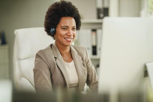 Shot of an African businesswoman wearing a headset while working on her computer during corona virus pandemic.