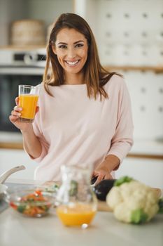 Shot of a young woman drinking fresh orange juice in her kitchen.