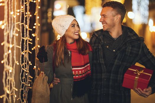 Shoot of a cheerful young couple are having fun in the city street at the Christmas night. They are laughing and buying presents for holidays to come.