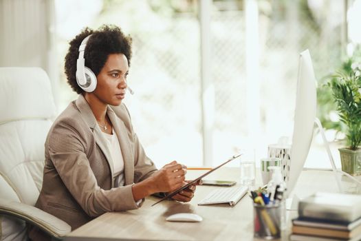 Shot of an attractive African businesswoman with headphones having video call while working on computer during corona virus pandemic.