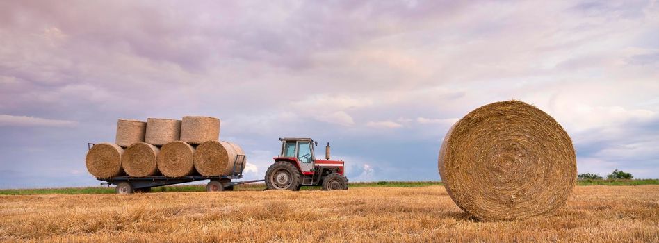 landscape with straw bales and tractor in french ardennes under cloudy sky during sunset in summer