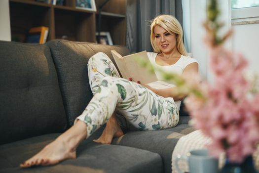 Shot of a beautiful young woman lying on the living room on the sofa, reading a book and relaxing at home.