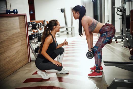 Shot of a muscular young woman in sportswear working out with female personal trainer at the gym.