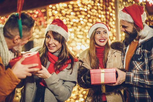 Shot of a group of cheerful young friends with Xmas gifts having fun at a night out.