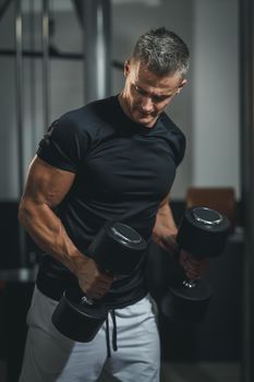 Shot of a muscular guy in sportswear working out at the hard training in the gym. He is pumping up triceps muscule with heavy weight.