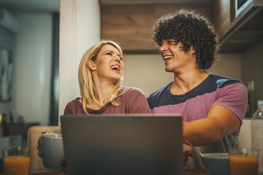 Shot of a happy couple using laptop together and eating breakfast before work in the kitchen.